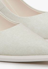 Licht beige flats met een gestructureerd oppervlak, met een puntige neus en een witte zool. Het materiaal is stof met een subtiel patroon.