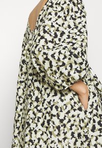 Zelené a černé vzorované oversized šaty s nafouknutými rukávy, bočním kapsou a volným, plynulým střihem. Hladká textura látky.