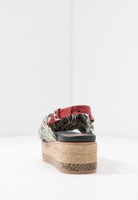 Sandale compensée avec plateforme en jute tissé, empeigne à motif noir et blanc, et boucle texturée rouge sur la bride de cheville, vue de dos.