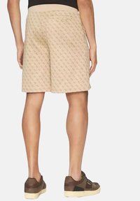 Pantalones cortos beige con un patrón geométrico, que presentan bolsillos y una textura suave. Combinados con zapatillas marrones sobre un fondo neutro.