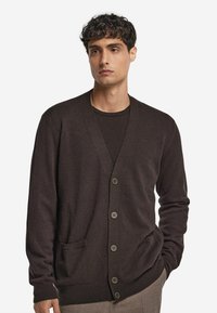 Brun cardigan i mjukt tyg, med V-hals, sex knappar, två fickor, ribbade ärmslut och mudd, slät textur och lös passform.