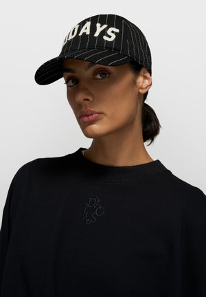 Casquette de baseball noire à rayures avec texte brodé blanc "DAYS" à l'avant ; portée avec un sweat-shirt noir comportant un petit motif brodé.