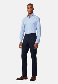 Camicia a scacchi blu chiaro, maniche lunghe, colletto con bottoni, abbinata a pantaloni navy e scarpe eleganti in pelle marrone.