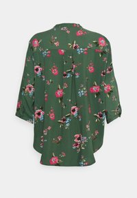 Blusa floral verde com uma mistura de flores rosas, vermelhas e azuis. Corte solto com mangas três quartos e detalhe de prega nas costas.