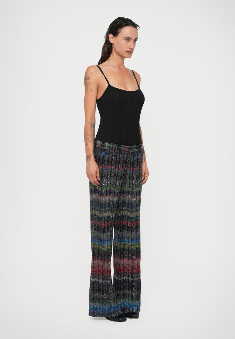 Haut noir sans manches associé à un pantalon large présentant un motif de rayures texturé multicolore. Le pantalon possède une taille élastique et des poches.