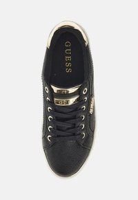 Schwarze Sneaker mit einem strukturierten Muster, goldfarbenen Akzenten und Logodetail an der Seite. Mit Schnürsenkeln und einer flachen weißen Sohle.