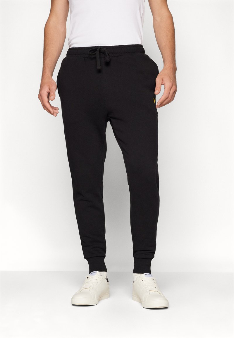 Schwarze Sweatpants aus Baumwolle, mit einem Kordelzugbund, schmal zulaufenden Beinen und einem kleinen gelben Logo auf der linken Seite.
