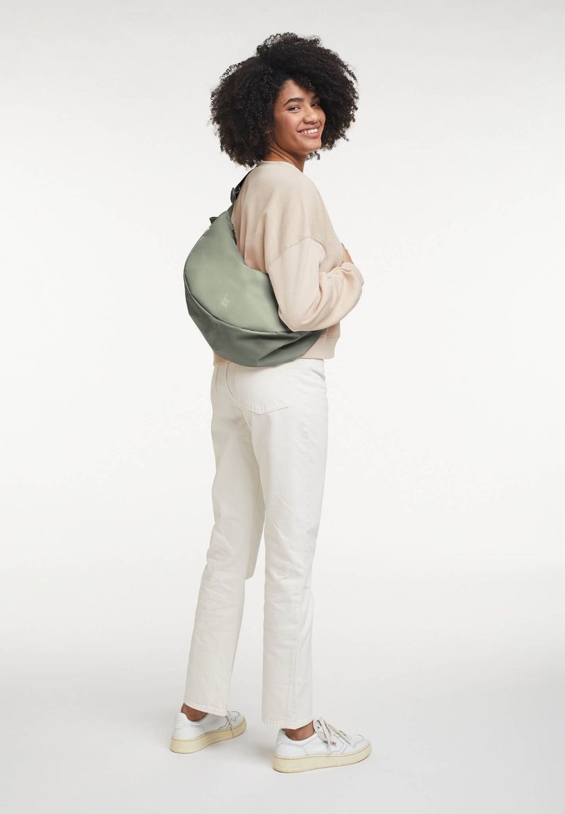Zaino verde slouchy realizzato in morbido materiale, con una tracolla arricciata e un design minimalista. Indossato a spalla da una persona.