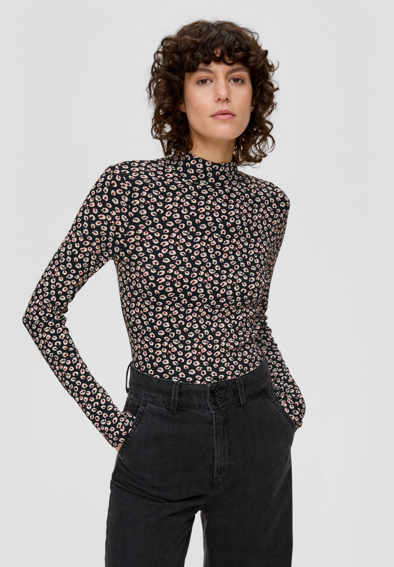 Czarna bluzka z długim rękawem i wysokim kołnierzem, zdobiona różowo-białym kwiatowym wzorem, w połączeniu z czarnymi spodniami o wysokim stanie. Gładka tekstura.