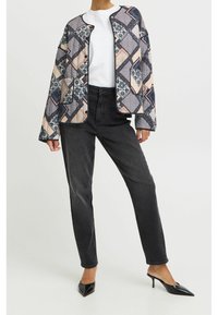 Quiltet jakke med patchwork-design i blå, beige og hvid, kombineret med sorte højtaljede jeans og sorte spidse hæle.