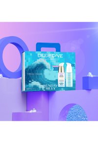 En teal boks mærket "Deep Dive Hydration Set" med to flasker: "Good Genes" og "Tidal." Kontrastfyldt baggrund i lilla geometriske former.