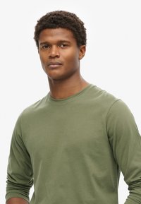 Camiseta de manga larga verde oliva, fabricada en una tela suave con un escote redondo y mangas ajustadas, que presenta una textura suave y un diseño minimalista.