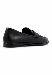 Mocassins en cuir noir avec une semelle plate, un bout rond et une texture lisse. Présente un détail de bande subtile sur le dessus.