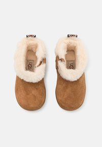 Brune mockasiner i nubuck med en kremfarget saueskinnsfôr og mansjett, med en liten dekorativ løkke på baksiden.