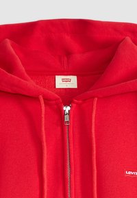 Sweat à zip rouge en tissu doux, avec une fermeture éclair argentée, un logo Levi's brodé et une capuche avec une doublure intérieure lisse.