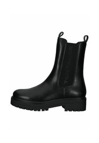 Botas negras de tobillo hechas de cuero, con paneles laterales elásticos y lengüetas de agarre. La suela gruesa y texturizada mejora el agarre y la estabilidad.