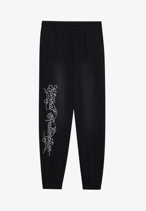 Pantalones de chándal negros con una cinturilla elástica, bolsillos laterales y un diseño gráfico en plateado en la pierna izquierda. Tejido suave con una textura lisa.