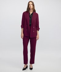 Traje burdeos que incluye un blazer de doble botonadura con botones plateados y pantalones ajustados, combinado con una camisa negra y tacones puntiagudos.