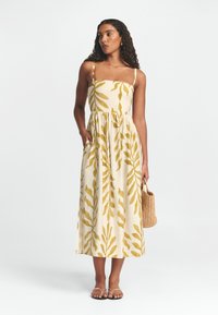 Kreemi kangast maxi kleit, millel on kollaste lehemustritega kaunistused, õhukeste rihmadega, lähedalt istuv talje ja kogutud vöökoht. Kootud kott ja sandaalid.