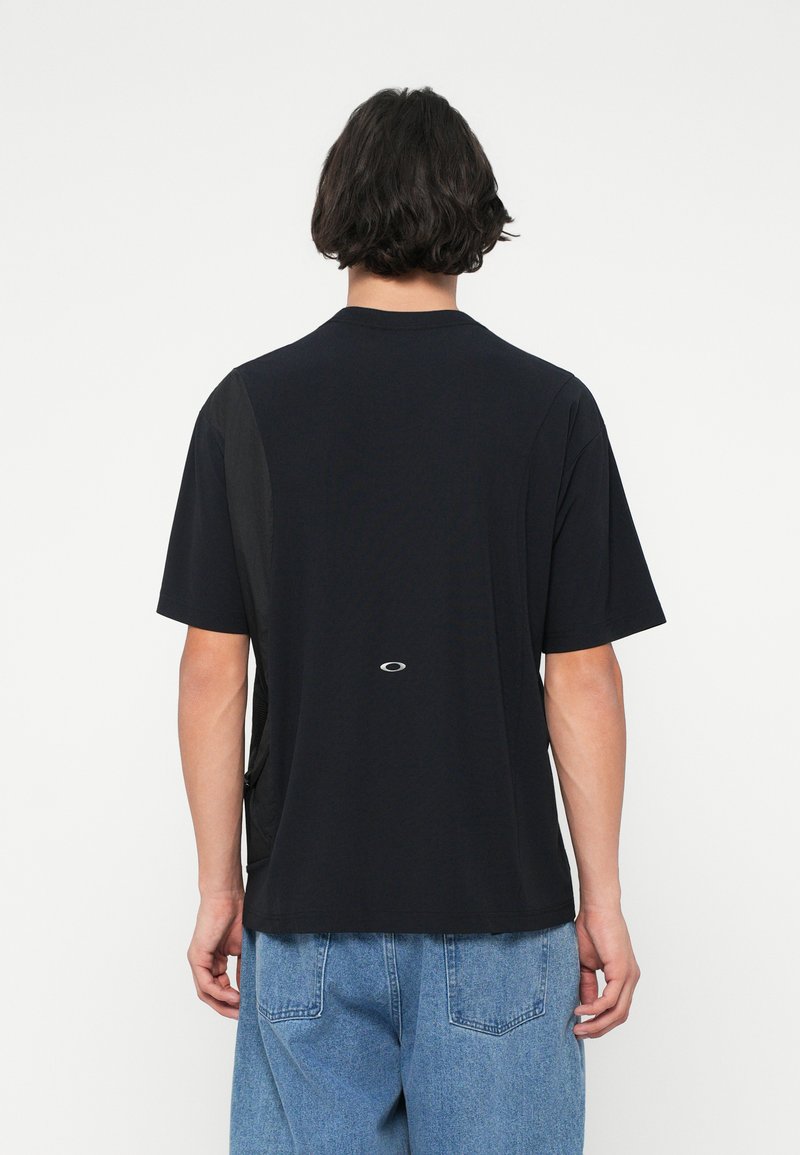 Schwarzes T-Shirt mit kurzen Ärmeln und Rundhals-Ausschnitt, mit seitlichen Einsätzen aus Mesh und einem kleinen Logo am unteren Rücken. Weicher Stoff mit lässiger Passform.