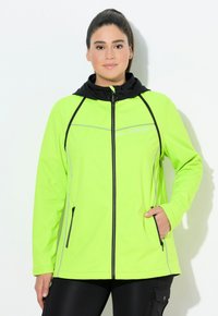 Neon vihreä vetoketjullinen takki mustalla hupulla, jossa on hopeiset yksityiskohdat, kaksi sivutaskua ja pehmeä, tekstiilinen kangas.