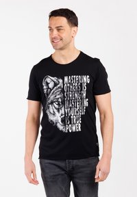Hombre con una camiseta negra que tiene la mitad de la cara de un lobo y el texto "Dominar a otros es fuerza. Dominarte a ti mismo es verdadero poder."