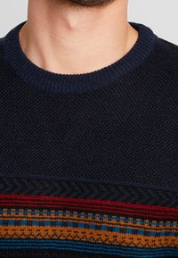 Pull en tricot marine avec une section supérieure texturée et une bande à motif horizontal comportant des rayures rouge, orange et bleue. Design à col rond.