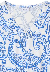 Camiseta blanca de cuello en V con estampado azul de paisley y pequeña etiqueta rectangular de tela con la inscripción "CECIL" cosida en el interior del cuello.