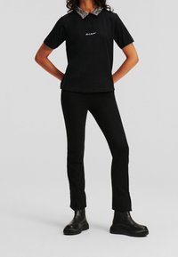 Černé polo tričko s vzorovaným límcem a vyšitým logem, doplněné černými slim-fit kalhotami a masivními černými kotníkovými botami.