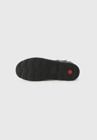 Black rubber shoe sole with textured zigzag pattern and circular red accent. Features durability and traction for various surfaces.