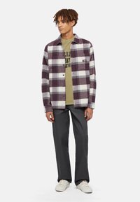 Plaid button-up shirt in shades of purple and white, with a chest pocket. Olive green T-shirt underneath. Grey trousers and white sneakers.