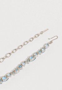Pulsera de cadena plateada con piedras azules en forma de lágrima incrustadas en un trabajo metálico intrincado, textura suave y acabado brillante, ajustable con un cierre de gancho.