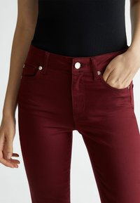 Bordowe rurki z przednimi kieszeniami, metalowym guzikiem oraz gładką fakturą, w połączeniu z dopasowanym czarnym topem.