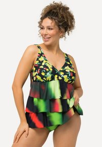 Blommig simtop med svart bakgrund, prydd med gula och röda blommor. Den nedre delen har överlappar av grönt och svart tyg med röda detaljer.