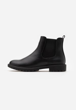 Bottine Chelsea en cuir noir avec panneaux latéraux élastiques, languette au talon et semelle basse à crampons sur fond blanc.