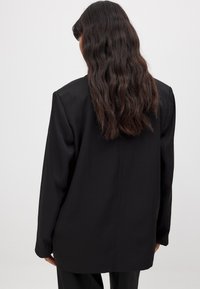 Mustern vaba, lõdva lõikega must jope, sileda tekstuuriga ja pikkade varrukatega. Lihtne disain ilma nähtavate sulgude või mustriteta.