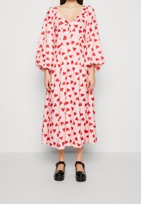 Kvinna iklädd en rosa midiklänning med röda hjärtan, puffade långa ärmar, knäppt byst, tillsammans med svarta Mary Jane plattformsskor.