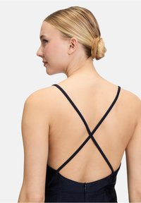 Bakvy av en ärmlös marinblå klänning med en djup V-ringning och korsade axelband, med en slät yta och dold dragkedja.