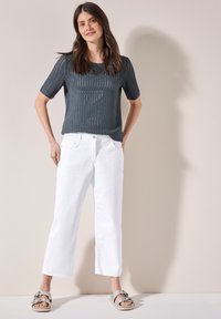 Top de manga corta de tejido abierto en gris oscuro, combinado con pantalones de pierna ancha blancos y sandalias gris claro con detalle decorativo de hebilla.