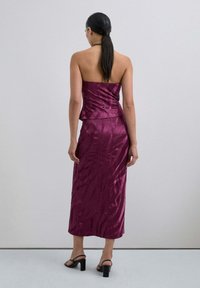 Vestido midi sin tirantes en satén burdeos profundo con un patrón ondulado texturizado y un detalle de peplum en la cintura, combinado con sandalias de tacón negras.