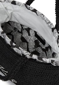 Fekete szőtt vámkosár, texturált külső felülettel, fehér bélés belsejével, amely fekete-fehér levélmintával van díszítve, és masszív fülekkel rendelkezik.