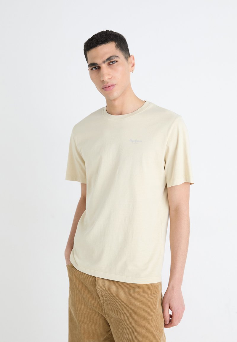 Crème-kleurige katoenen t-shirt met een ronde hals en korte mouwen. Heeft een klein logo in lichtblauw op de borst. Eenvoudige, relaxte pasvorm.
