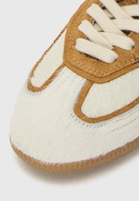 Sneaker featuring a cream fur upper with brown suede accents. Shape is round at the toe with beige laces and a textured rubber sole.