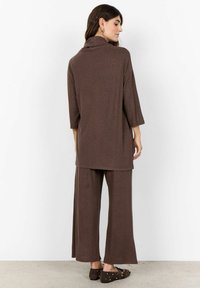 Completo due pezzi marrone composto da una lunga tunica con collo a cerchio e pantaloni a gamba larga. Tessuto morbido con un delicato motivo melange.
