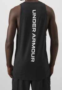 Débardeur noir sans manches avec un grand logo blanc "UNDER ARMOUR" disposé verticalement dans le dos, fabriqué à partir d'un tissu lisse et léger.