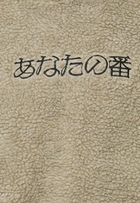 Beige fleece stof med en fluffy struktur, der har sort broderet tekst. Overfladen ser blød og varm ud.