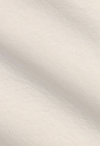 Gros plan sur un tissu beige clair avec une texture en tissage diagonal fin et un léger ombrage.