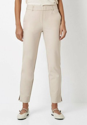 Beige tailored pants with a smooth texture, featuring a mid-rise elastic waistband, side pockets, and slight slits at the ankles.