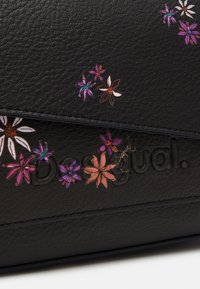 Svart läderväska med färgglad blommönstring i lila, rosa och vitt. Varumärket "Desigual" är präglat på materialet.