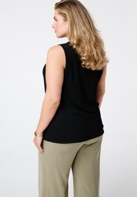 Zwart geribde mouwloze top met een ronde halslijn, gecombineerd met losse olijfgroene broek. Haar is gestyled in losse krullen.